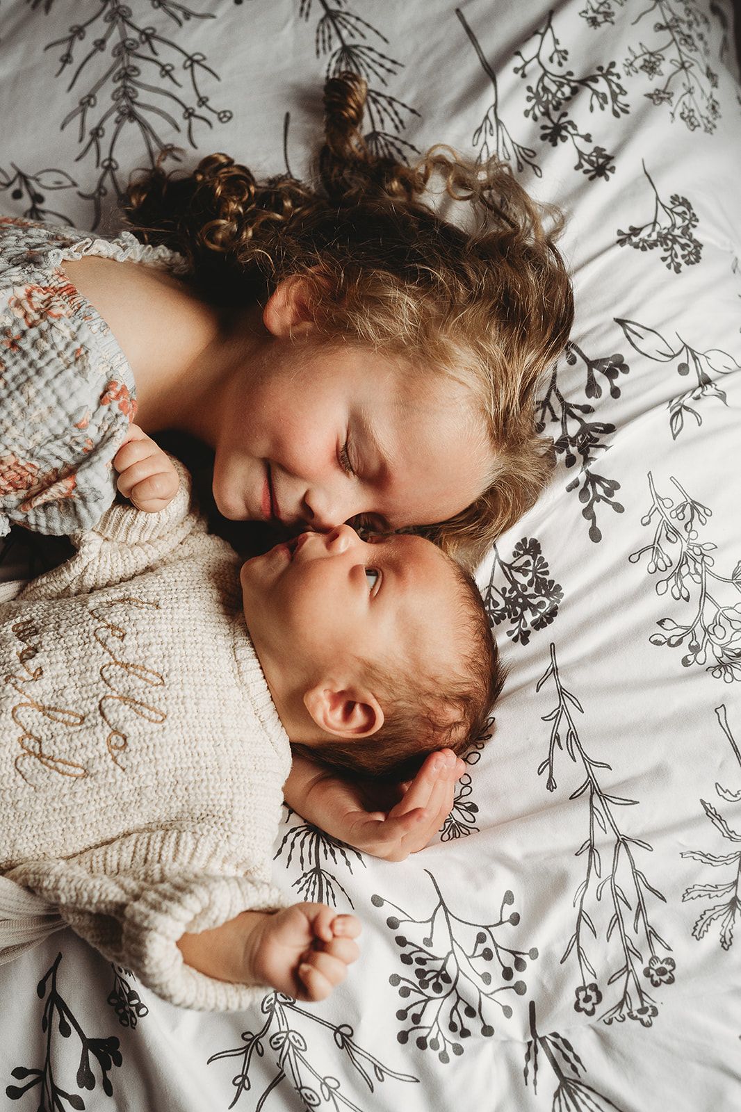 Tender moment between parent and baby lying on floral patterned bedding.