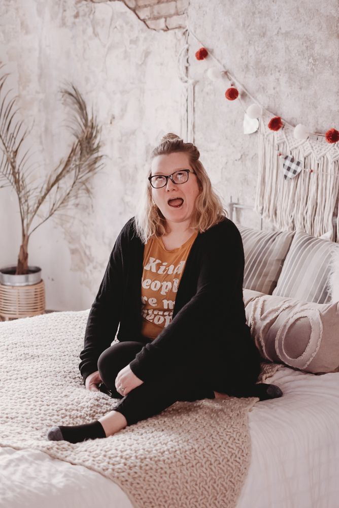 Woman in black relaxing on a textured white bedspread with boho decor.