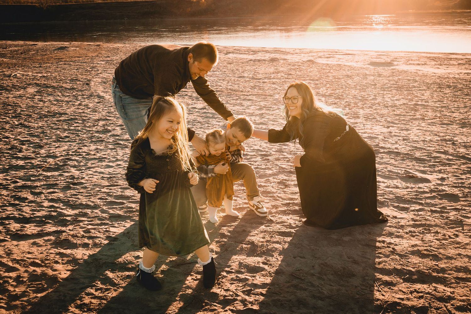 Group plays and laughs together on beach during golden hour with sun flare.