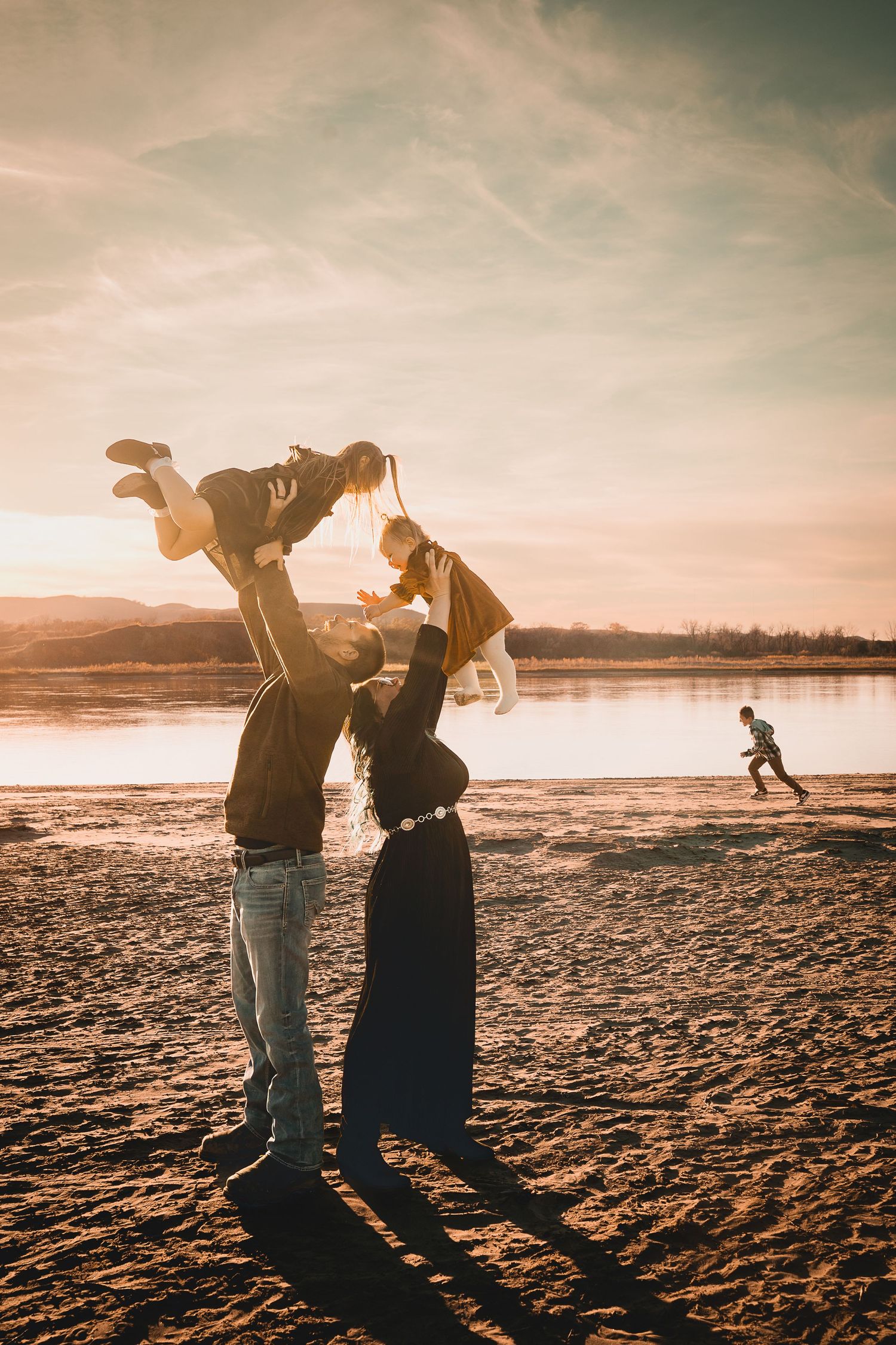 A family laughs and giggles along the banks of the Missouri River at sunset during a fall petite family session near Bismarck, ND