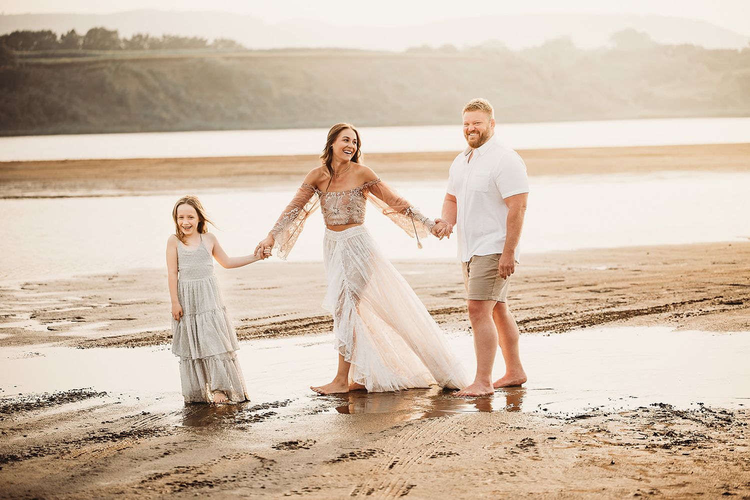 Family enjoys sunset moments together on a sandy beach with golden light and waves in the background.