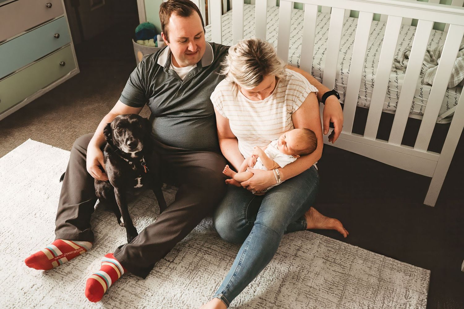 Cozy family moment at home with pet dog beside white crib.