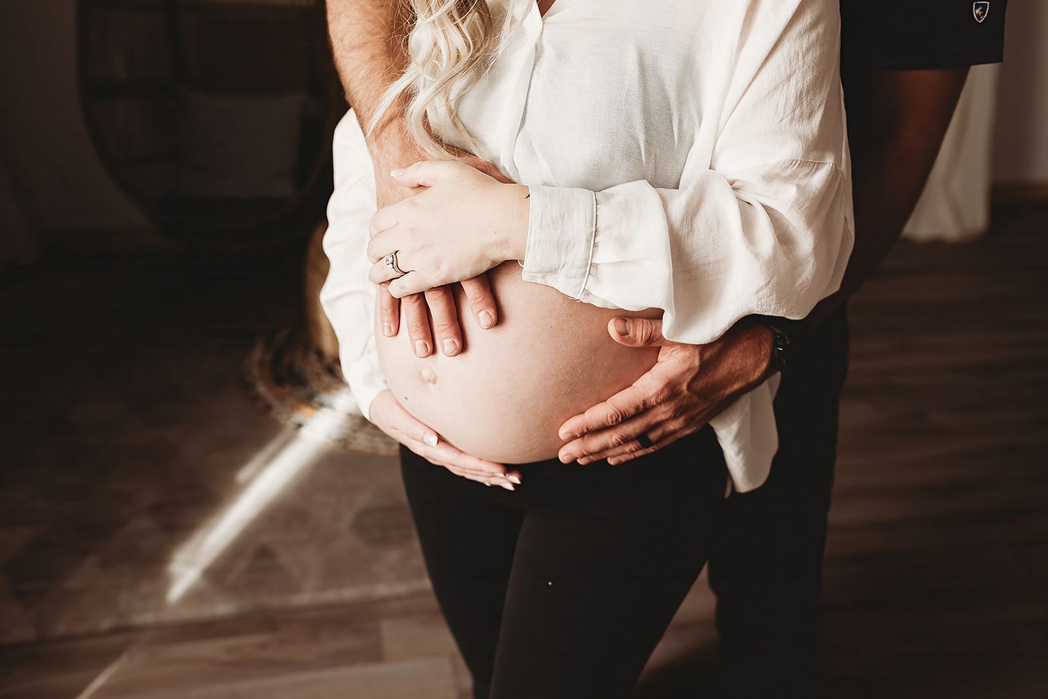 Close-up view of hands gently cradling a pregnant belly in white clothing.
