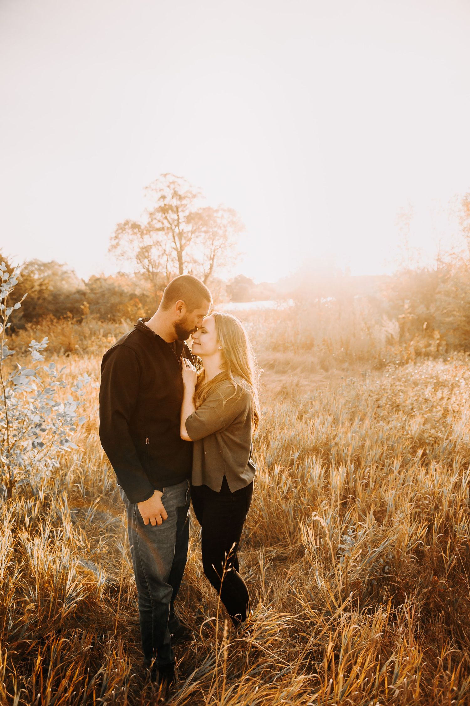 Intimate couple portrait in sunlit field with golden grass and soft lighting.